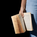 Eine Frau vor einem schwarzen Hintergrund hält ein aufgeschlagenes Buch in der Hand.
