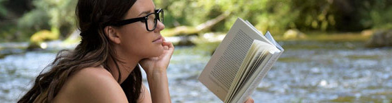 Eine Frau sitzt am Fluss und liest ein Buch.