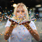 Eine Frau pustet Konfetti aus einem Buch in Richtung Kamera.