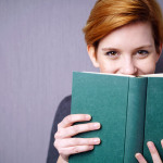 Lachende Frau versteckt sich hinter einem Buch.
