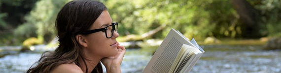 Eine Frau sitzt am Fluss und liest ein Buch.