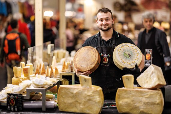 Ein Messeverkäufer hält zwei Käselaibe in der Hand