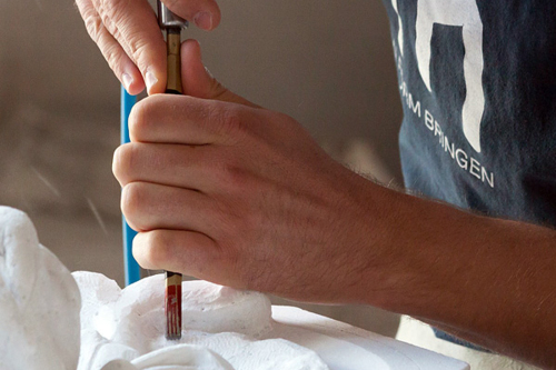 Nahaufnahme der Hände eines Bildhauers. Mit einem Werkzeug fräsen sie eine Form in einen Steinblock.