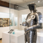 Handwerk-Raum im Stadtmuseum im Fembohaus in Nürnberg. Im Vordergrund rechts befindet sich eine mannshohe Vitrine mit einer silbernen Ritterrüstung inklusive Helm. Im Hintergrund befinden sich weitere Vitrinen mit Handwerk.