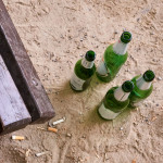 Leere Bierflaschen stehen vor einer Parkbank auf dem Boden.