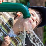 Kind trinkt Wasser aus Pumpbrunnen.