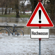 Warnschild Hochwasser vor einem überfluteten Gebiet.