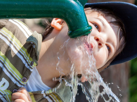 Das Bild zeigt ein Kind beim Trinken aus einem Pump·brunnen.