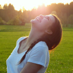 Lachende junge Frau in einer grünen Landschaft bei untergehender Sonne.