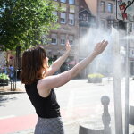 Eine Frau kühlt sich unter dem kühlen Wassernebel einer Sprühnebelsäule.