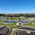 Blick vom Faulturm auf das Klärwerk I in Nürnberg auf vier kreisrunde Reinigungsbecken, gefüllt mit graubraunem Wasser.