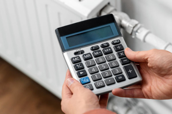 Foto von einem Taschen·rechner und einer Hand vor einer Heizung.