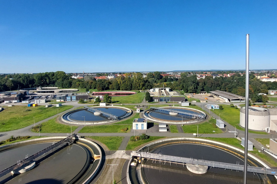 Blick vom Faulturm auf das Klärwerk I in Nürnberg auf vier kreisrunde Reinigungsbecken, gefüllt mit graubraunem Wasser.