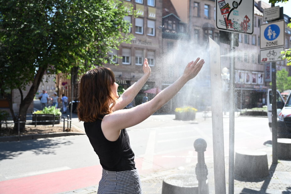 Eine Frau kühlt sich unter dem kühlen Wassernebel einer Sprühnebelsäule., Bild © Christine Dierenbach / Stadt Nürnberg
