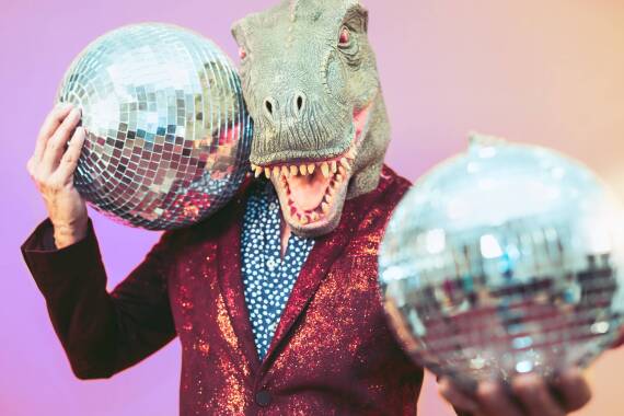 Ein Mensch mit T-Rex-Maske hält zwei Discokugeln.