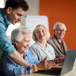 Eine Gruppe Senioren wird an Laptops von einem Tutor betreut.