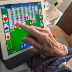 Eine Seniorin spielt ein Kartenspiel auf einem Tablet.