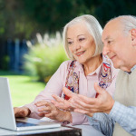 Ein älteres Paar sitzt vor einem Laptop.