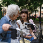 Enkeltochter und Oma mit Gehhilfe verbringen gemeinsame Zeit im Park auf einer Bank