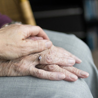 Eine Hand liegt auf den Händen einer alten Frau.