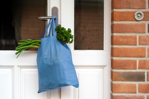 Blaue Einkaufstüte mit frischem Gemüse an einer Tür hängend.