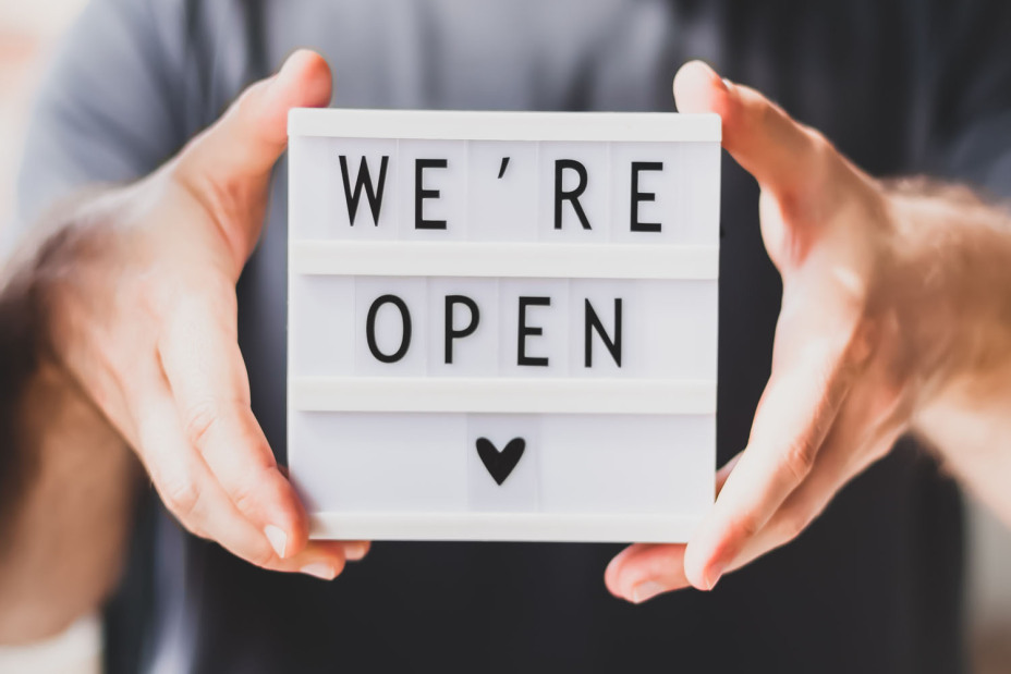Ein Mann hält eine kleine Lightbox mit dem Schriftzug "We're open" in die Kamera.