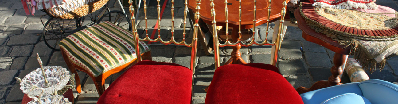 Bild, das verschiedene alte Möbelstücke zeigt. Zwei rot-goldene Stühle, einen antiken kleinen Tisch und verschiedene Geschirr Teile