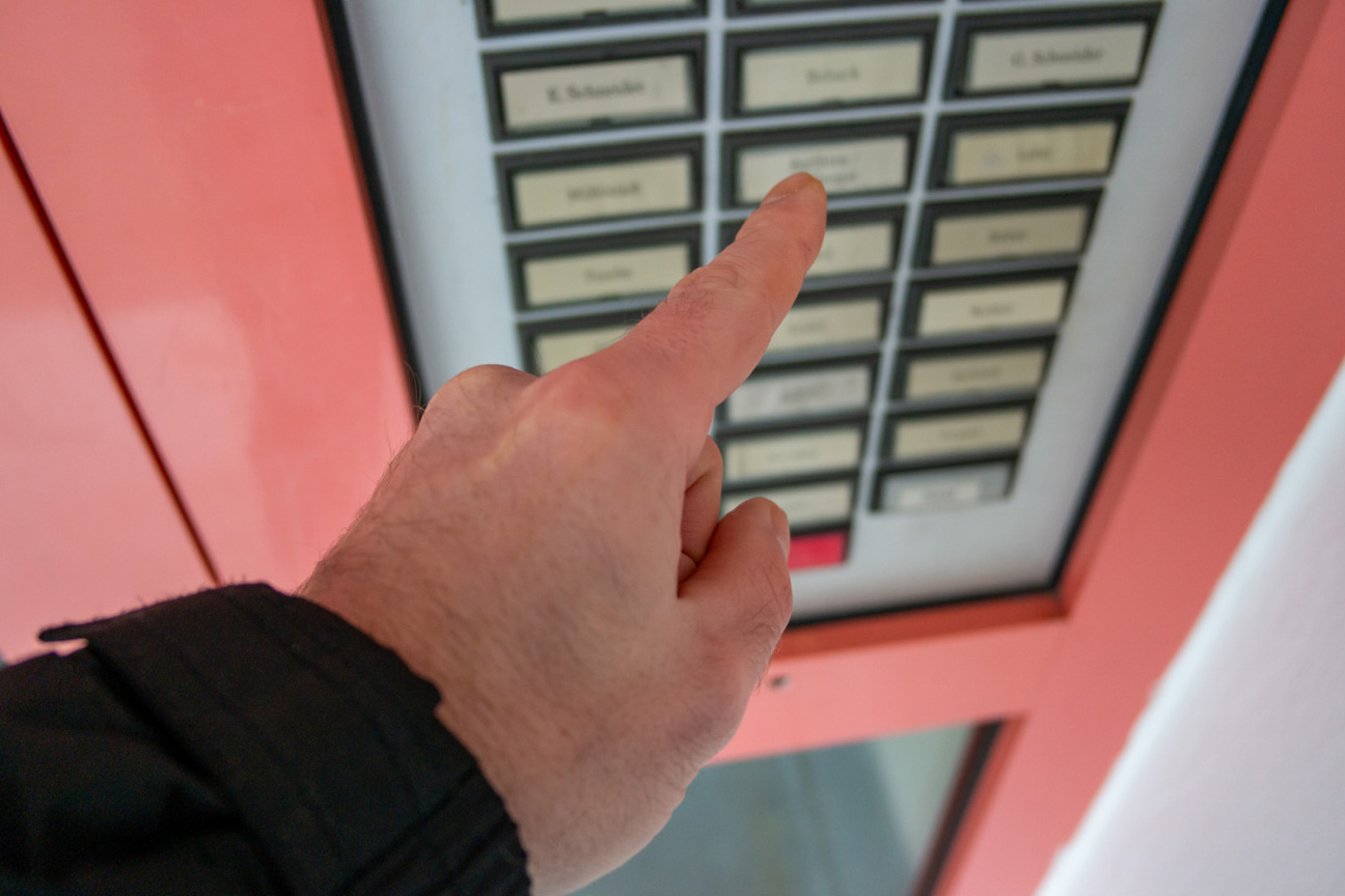 Ein Mann klingelt an der Haustür eines Mehrfamilienhauses., Bild © Adobestock/1214669275