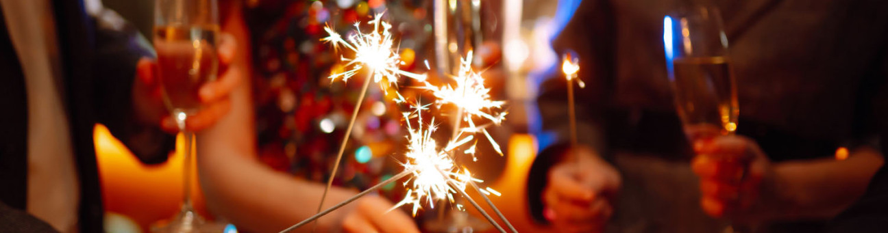 Leute in festlicher Kleidung halten auf einer Party Wunderkerzen und gefüllte Sektgläser in den Händen.