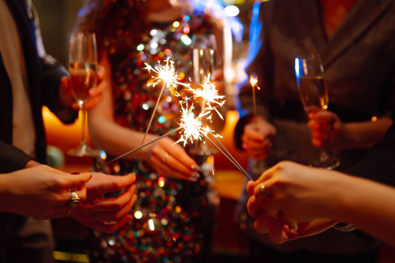 Leute in festlicher Kleidung halten auf einer Party Wunderkerzen und gefüllte Sektgläser in den Händen., Bild © Maxbelchenko / AdobeStock