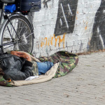 Obdachloser Mann liegt in einem Schlafsack auf der Straße.