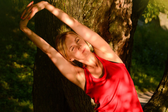 Frau macht im Freien unter einem Baum eine Yogaübung.