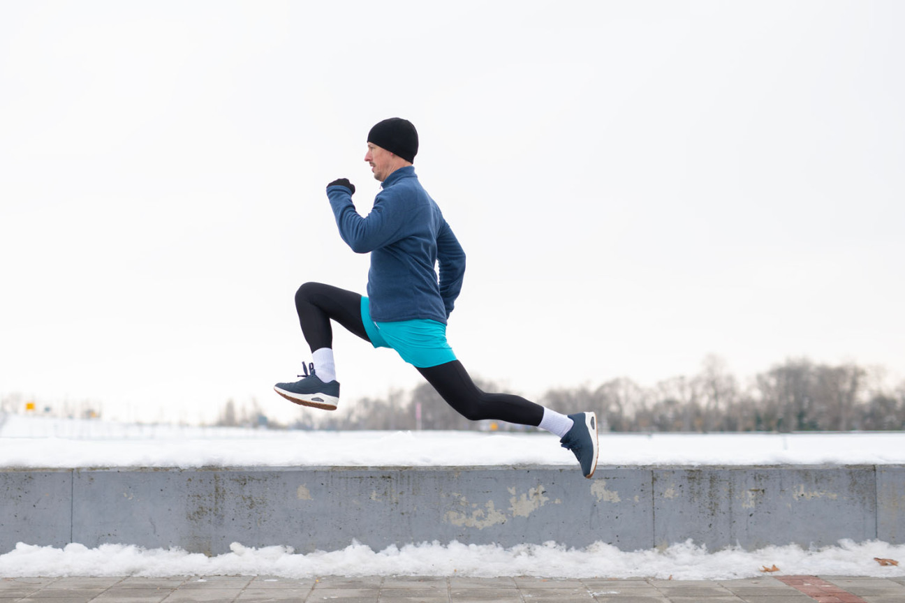 Ein Mann joggt im Winter einen verschneiten Gehweg entlang., Bild © Dexon Dee / AdobeStock