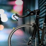 Fahrrad an Hauswand im Dunkeln mit Lichtern im Hintergrund.