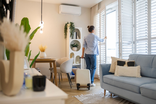 Eine Frau ist gerade in einer Ferienwohnung angekommen. Im Vordergrund steht ihr noch nicht ausgepackter Koffer.