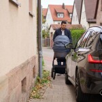 Ein Mann schiebt einen Kinderwagen und versucht, an einem auf dem Gehweg parkenden Auto vorbeizukommen.