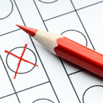 Symboldbild für Wahlen: Ein roter Buntstift und ein rotes Kreuz in einem Feld.