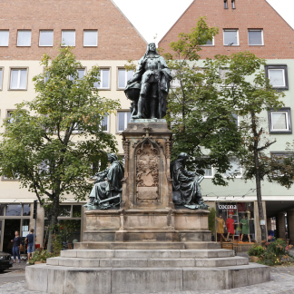 Auf dem Theresienplatz thront in seiner ganzen Pracht die Statue Martin Behaims. Nicht ganz so prachtvoll verstecken sich dahinter drei Berg-Ahorne. 