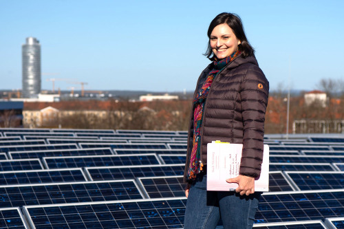 Christina Röthlein vom Liegenschaftsamt steht auf einem Dach mit Solarmodulen. © Christine Dierenbach / Stadt Nürnberg