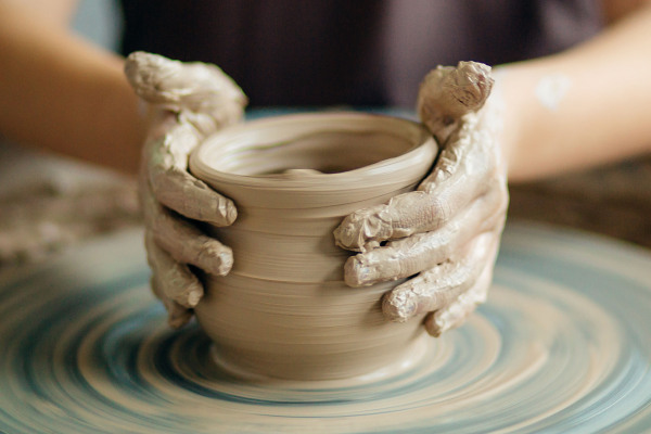 Zwei tonbeschmierte Hände formen aus einem Stück Ton auf einer Drehscheibe ein Gefäß.