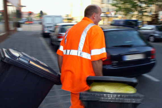Ein Mitarbeiter der Müllabfuhr rollt Mülltonnen an den Straßenrand.