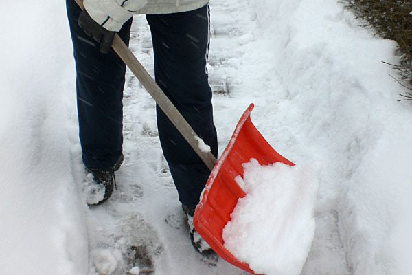 Person schippt mit einer Schneeschaufel den Gehweg frei.